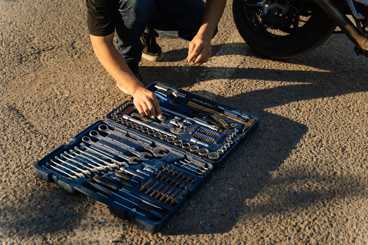 A mechanic works on a motorcycle using a comprehensive toolset outdoors in daylight.