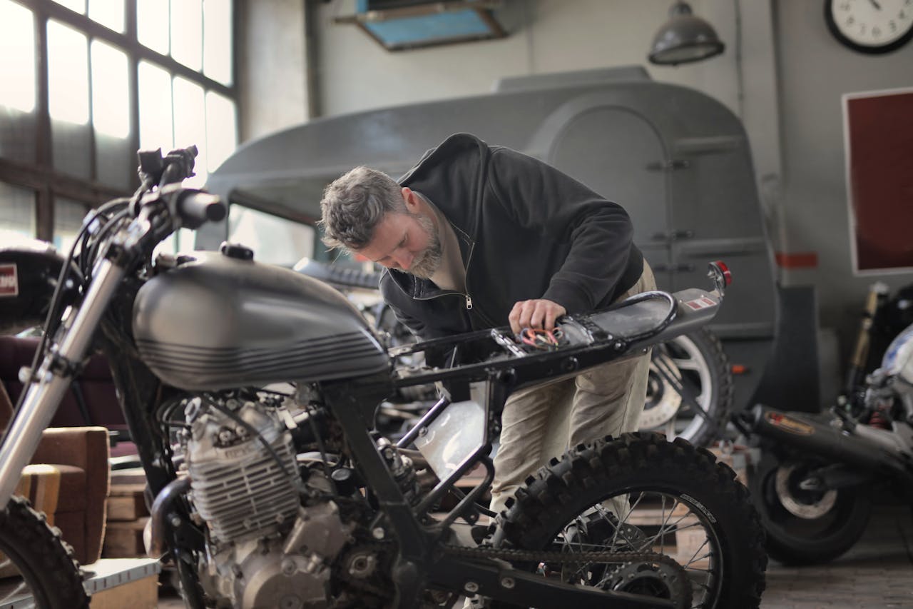 An adult male mechanic working on a motorcycle inside an industrial style workshop.