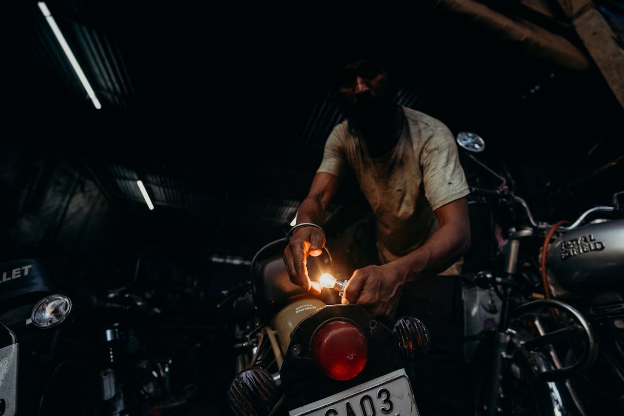 A mechanic working on a motorcycle bulb in a dimly lit repair shop.